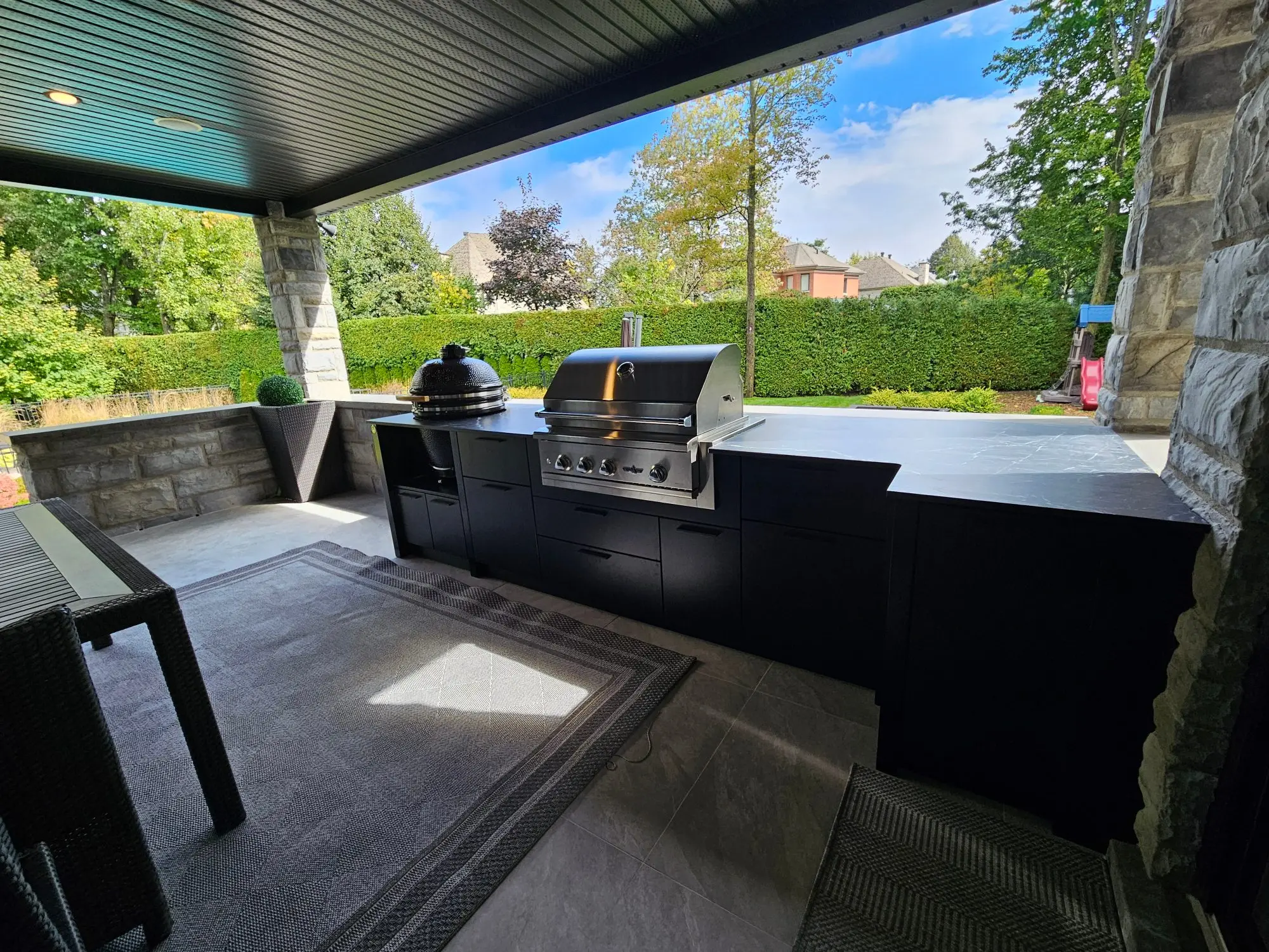 Cuisine extérieure sur mesure noire avec gril intégré, installée sous un abri de terrasse couvert dans une cour arrière du Grand Montréal
