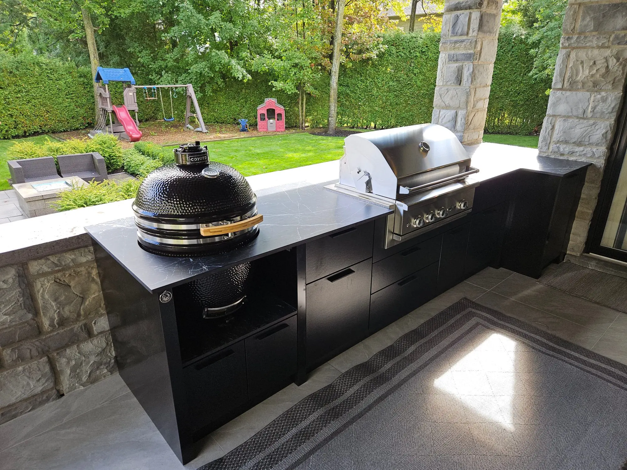 Terrasse avec BBQ intégré : cuisine extérieure noire avec gril au gaz et fumoir kamado encastrés dans une cour arrière familiale