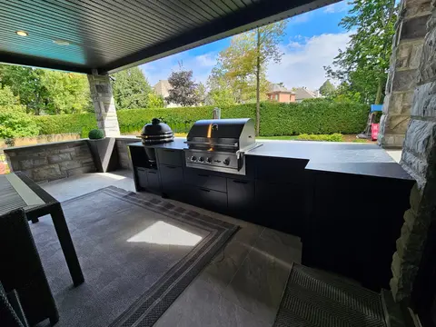 Cuisine extérieure sur mesure noire avec gril intégré, installée sous un abri de terrasse couvert dans une cour arrière du Grand Montréal