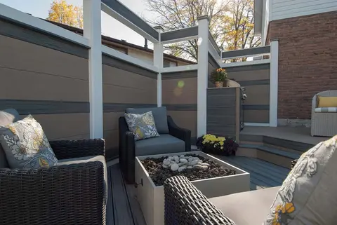 Foyer extérieur au propane à cuve rectangulaire en béton entouré de fauteuils en résine tressée sur une terrasse composite