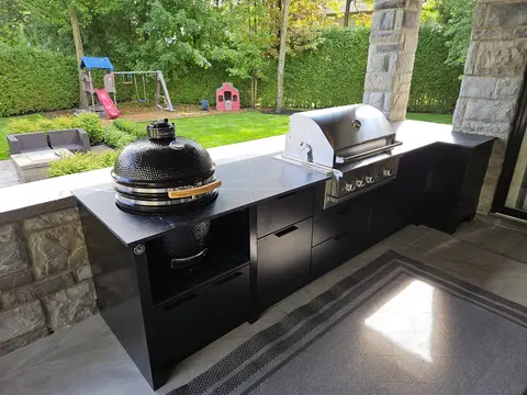 Terrasse avec BBQ intégré : cuisine extérieure noire avec gril au gaz et fumoir kamado encastrés dans une cour arrière familiale